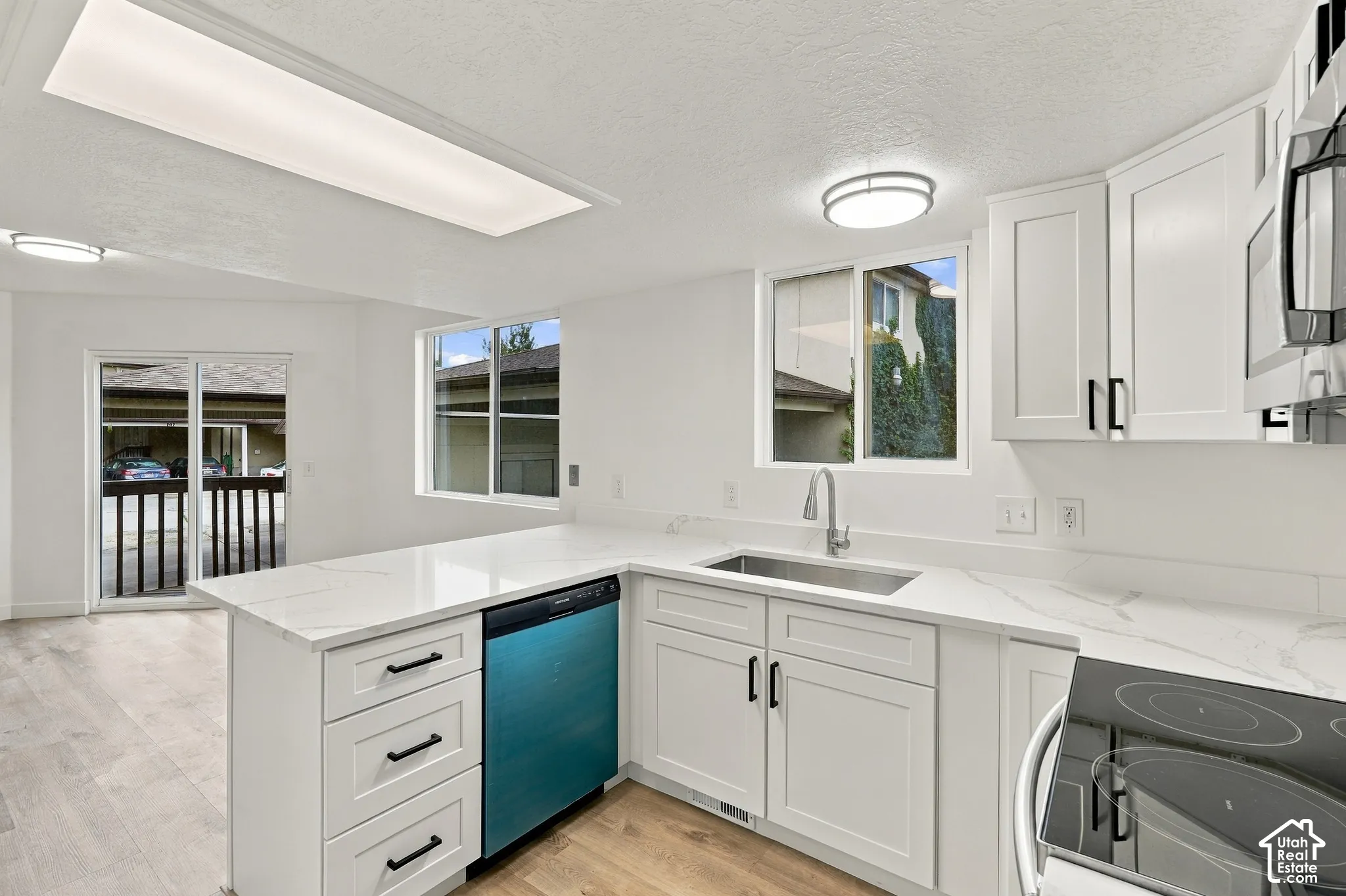 Modern kitchen featuring white shaker-style cabinetry, white countertops, stainless steel sink with gooseneck faucet, and wood-finish flooring