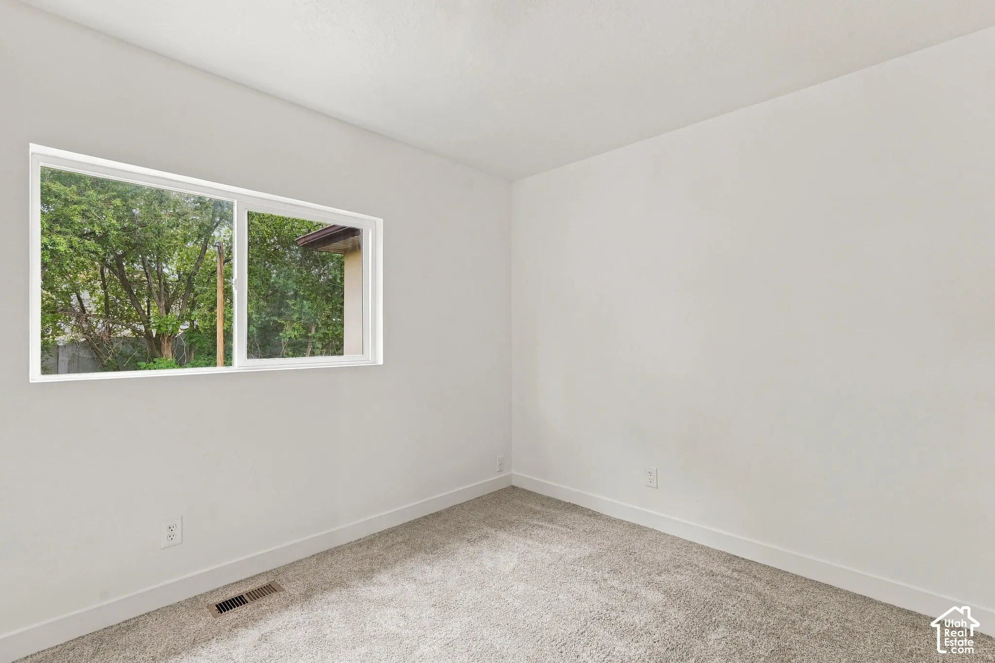 Light-colored carpeting, white painted walls, and a large window
