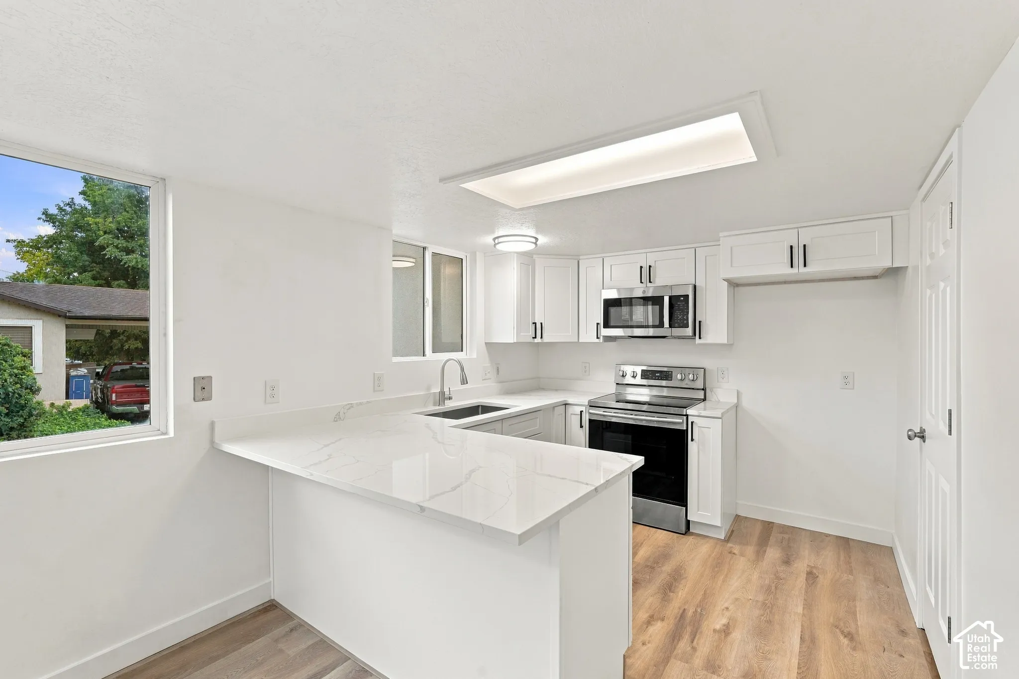 Kitchen featuring white cabinetry, stainless steel appliances, wood-finish flooring, white countertops, and recessed lighting