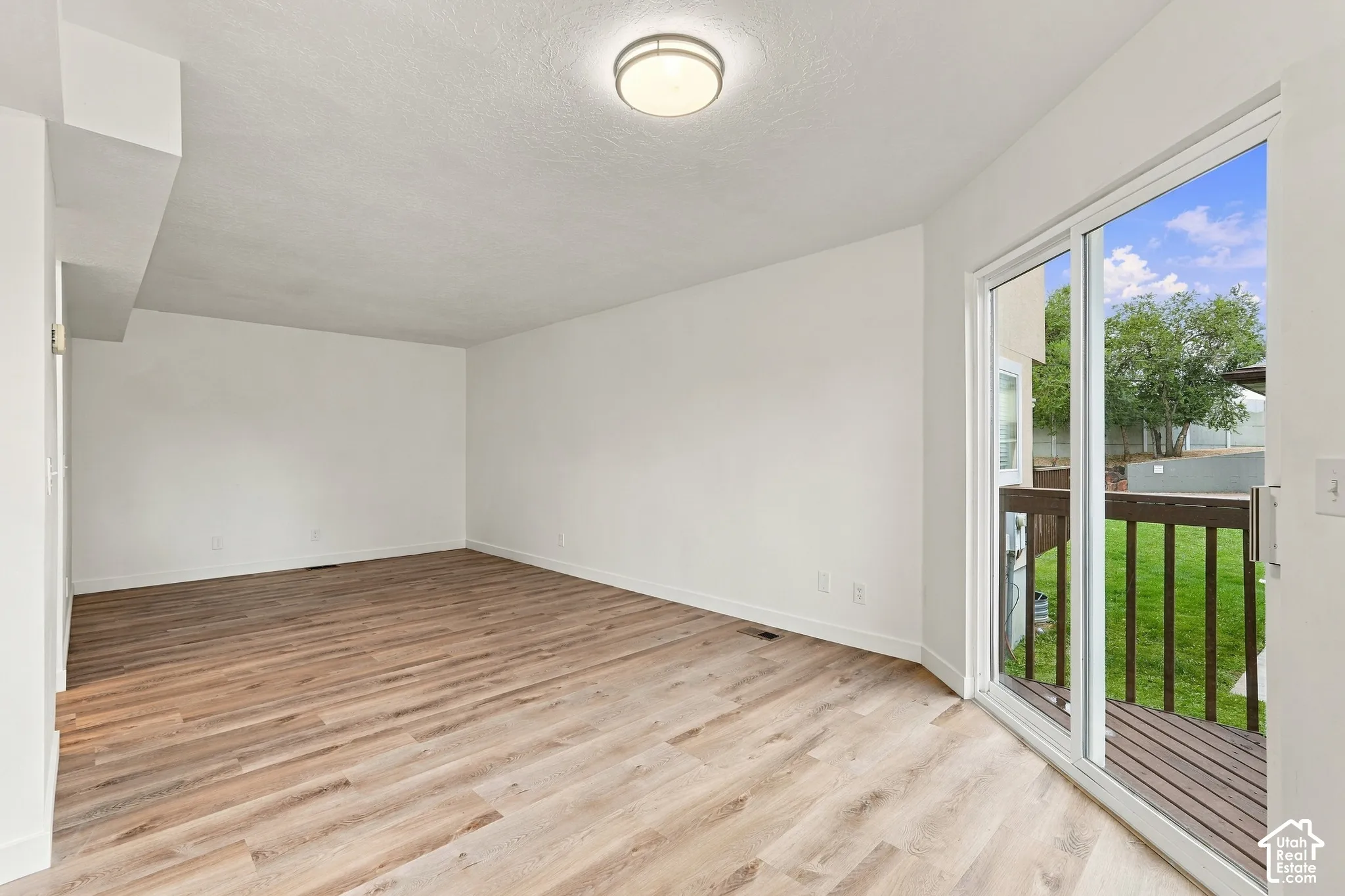 Wood-finish flooring, white walls, flush mount ceiling light, sliding glass door, and an exterior deck with railings