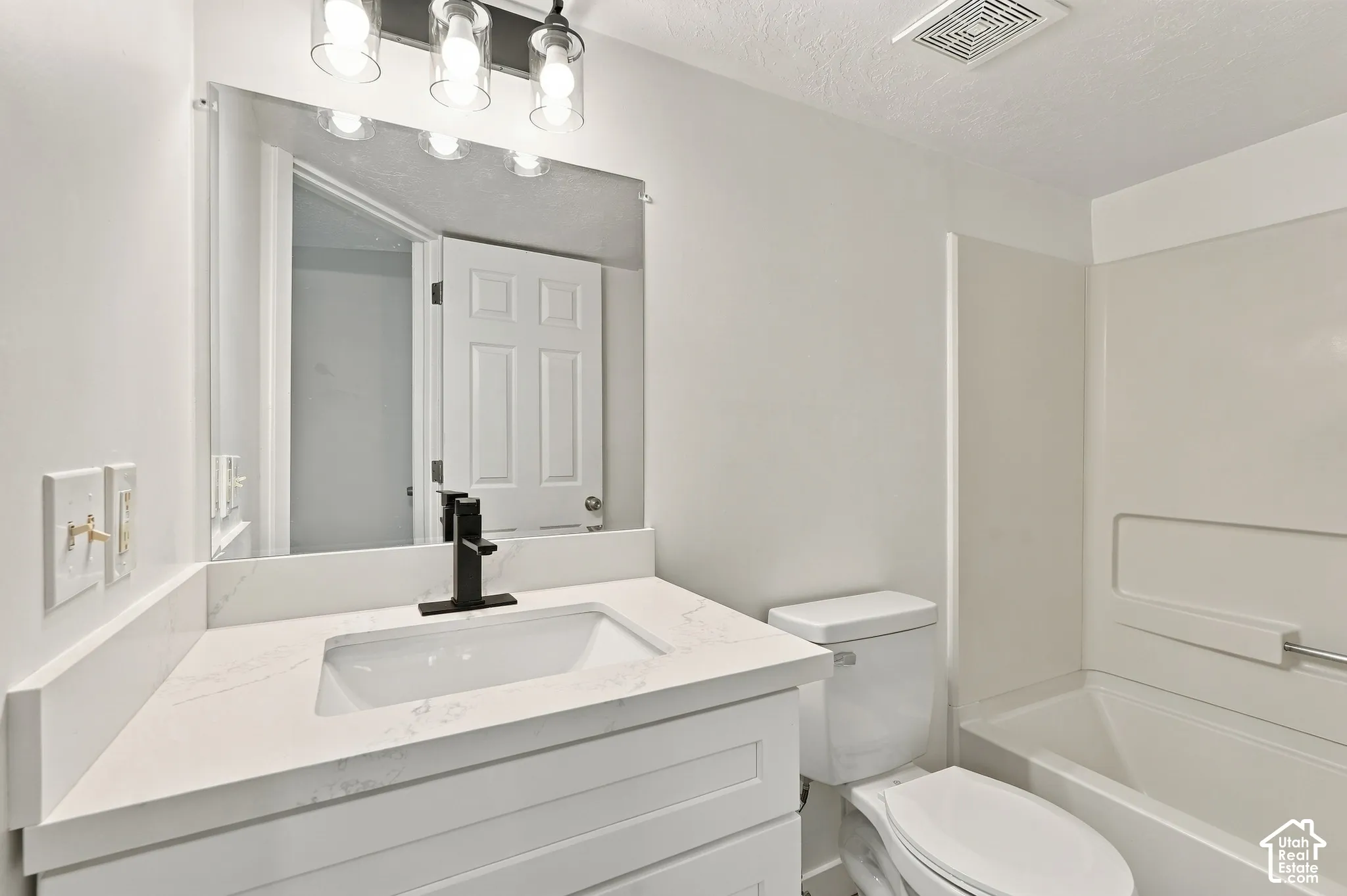 White vanity with a rectangular sink, matte black faucet, and stone-finish countertop
