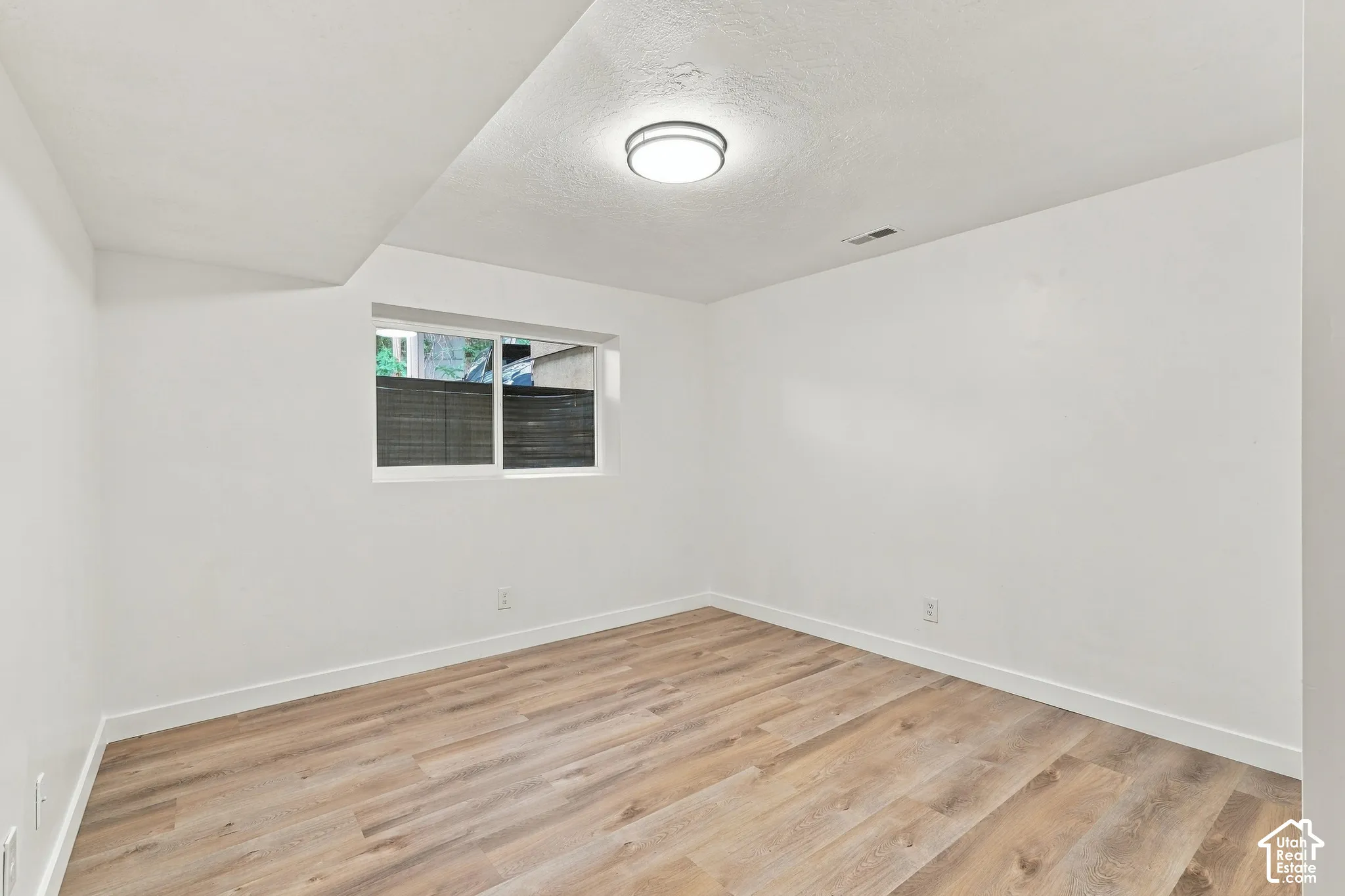 Wood-finish flooring, white walls, and a flush-mount ceiling light