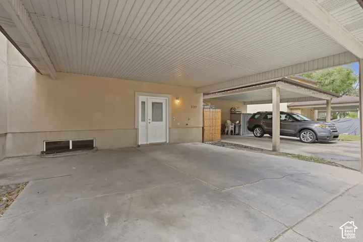 Covered carport, stucco exterior, concrete driveway, white entry door, exterior wall sconce