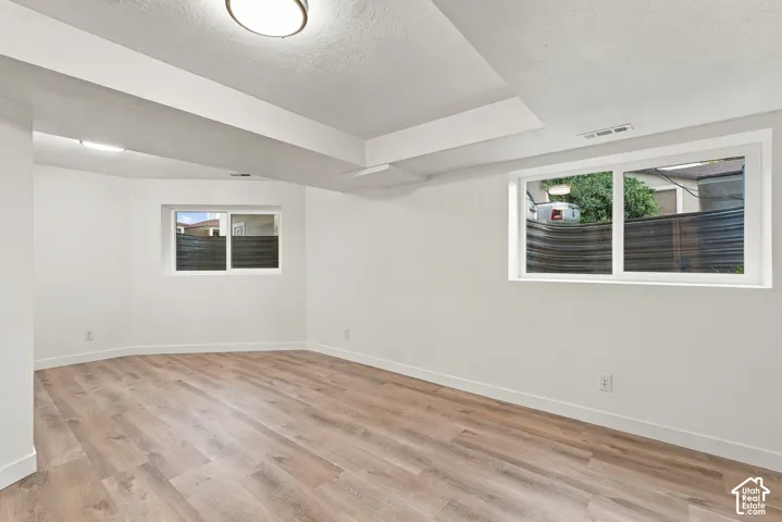 Expansive room with neutral white walls, wood-finish flooring, recessed ceiling fixture, and dual windows providing natural light