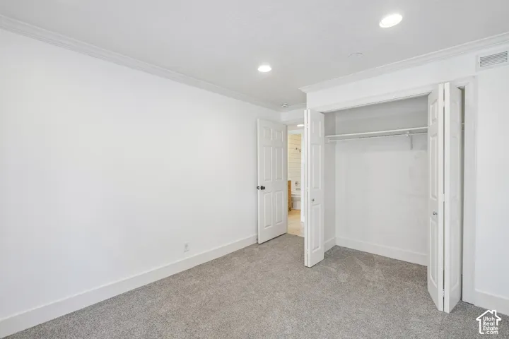 Light gray carpet flooring, white walls, white bi-fold closet doors, recessed lighting, and crown molding