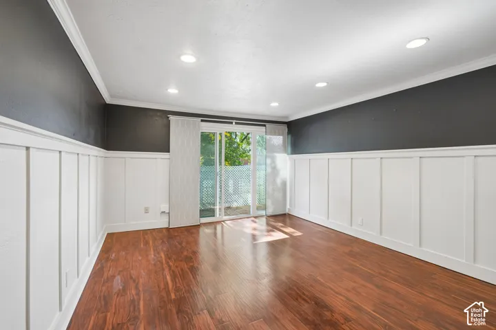 Wood-finish flooring, white wainscoting, recessed lighting, crown molding, and sliding glass door