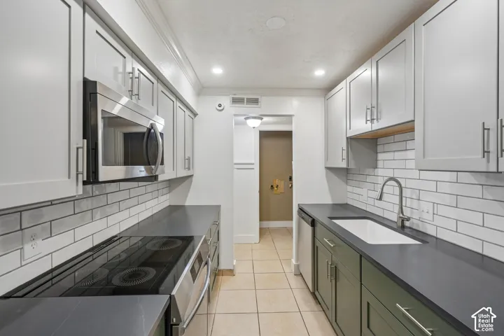 Kitchen featuring white subway tile backsplash, light grey upper cabinetry, dark green lower cabinetry, dark countertops, and stainless steel appliances
