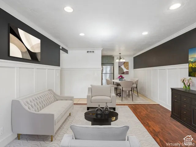 Recessed lighting, crown molding, two-tone walls with wainscoting, wood-finish flooring, and a dining area with a chandelier