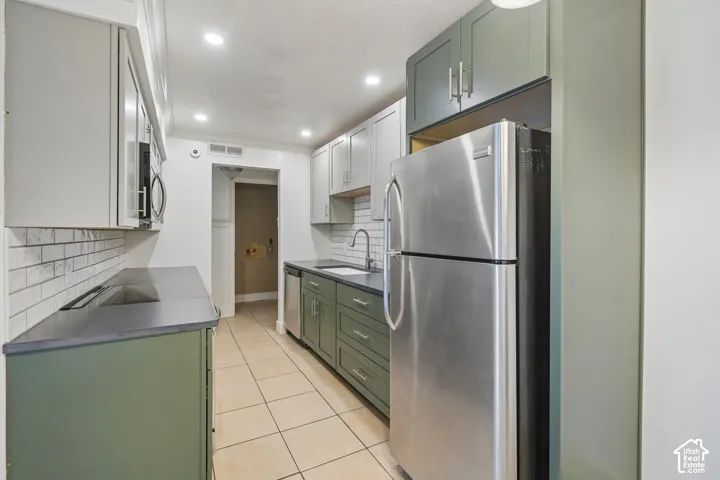 Galley kitchen featuring dual-toned cabinetry, stainless steel appliances, a white subway tile backsplash, dark countertops, and recessed lighting