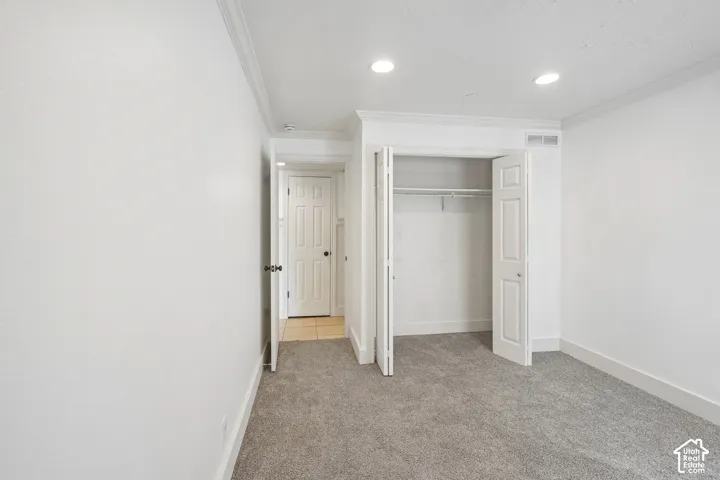 Recessed lighting, crown molding, gray carpet flooring, white bi-fold closet doors, and a paneled interior door