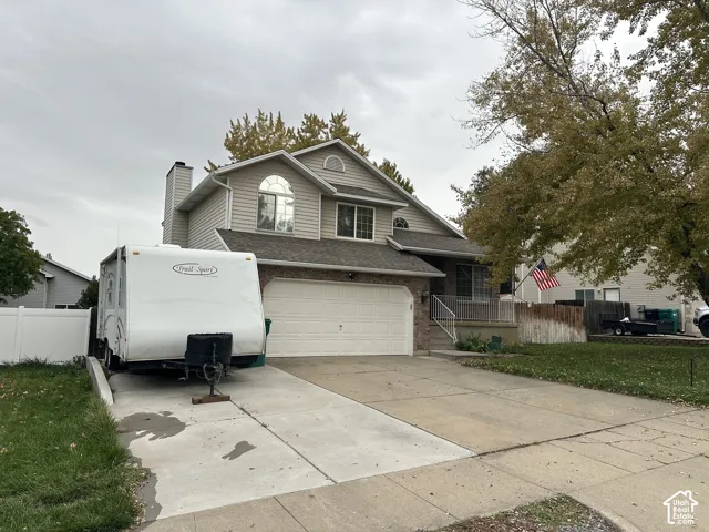 Two-story exterior with horizontal siding and brick veneer, attached two-car garage, concrete driveway with side parking, and white vinyl privacy fencing