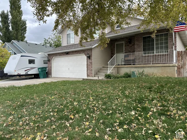 Split-level exterior featuring a brick and horizontal siding facade, a two-car garage, and a covered concrete porch with a white metal railing