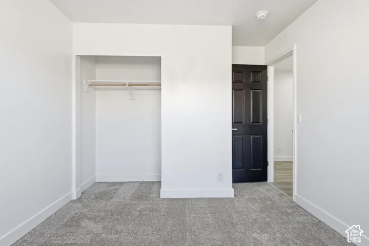 Bedroom featuring neutral wall paint, gray carpet flooring, a black paneled door, and a dedicated closet space with shelving