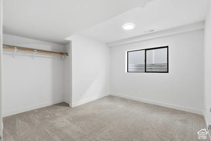 Bedroom featuring neutral wall paint, gray carpet flooring, a black paneled door, and a dedicated closet space with shelving