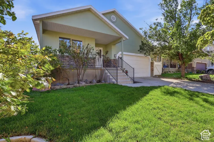 Rambler with stone accent siding, covered entry porch, concrete driveway, attached garage, and a lush lawn