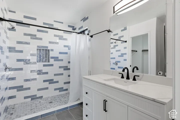 White vanity with a solid surface countertop, matte black fixtures, large tiled walk-in shower