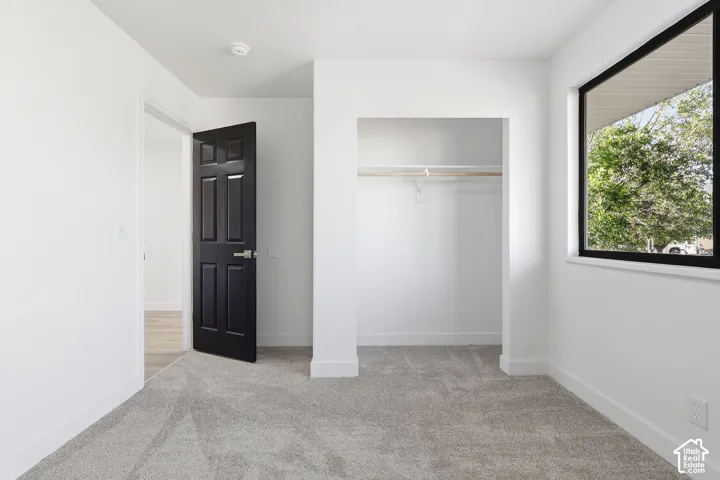 Bedroom featuring neutral wall paint, gray carpet flooring, a black paneled door, and a dedicated closet space with shelving