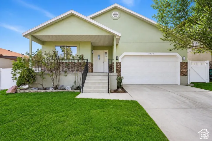 Rambler with stone accent siding, covered entry porch, concrete driveway, attached garage, and a lush lawn