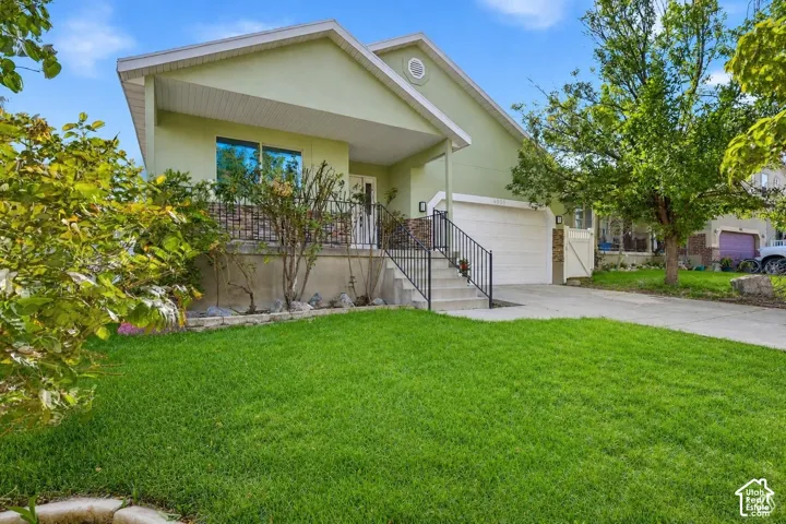 Rambler with stone accent siding, covered entry porch, concrete driveway, attached garage, and a lush lawn