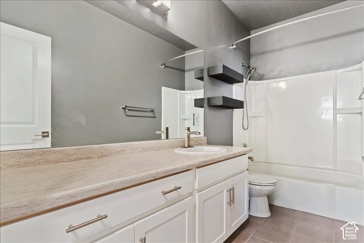 White shaker-style cabinetry with brushed nickel hardware, large vanity mirror, built-in floating shelves, white tub with shower, and tile flooring