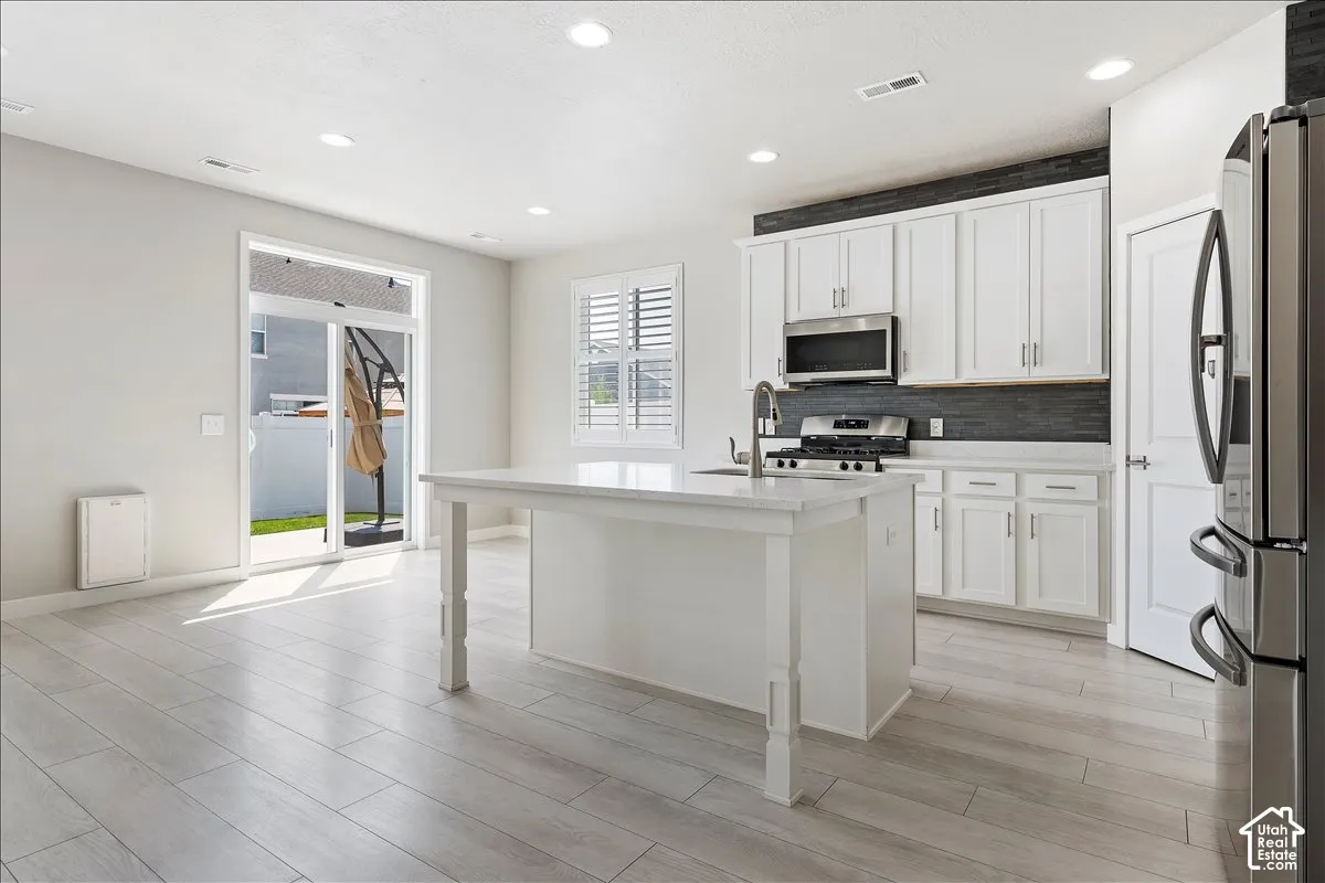 Kitchen featuring white shaker cabinetry, stainless steel appliances, a center island, and a dark tile backsplash