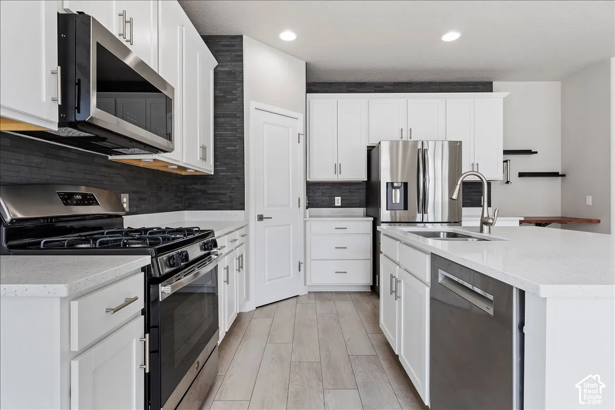 Kitchen featuring white cabinetry, stainless steel appliances, light-toned countertops, a dark tile backsplash, and wood-finish flooring