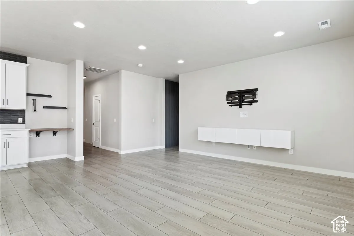 Recessed lighting, wood-finish flooring, built-in shelving, white cabinetry, and a floating media console