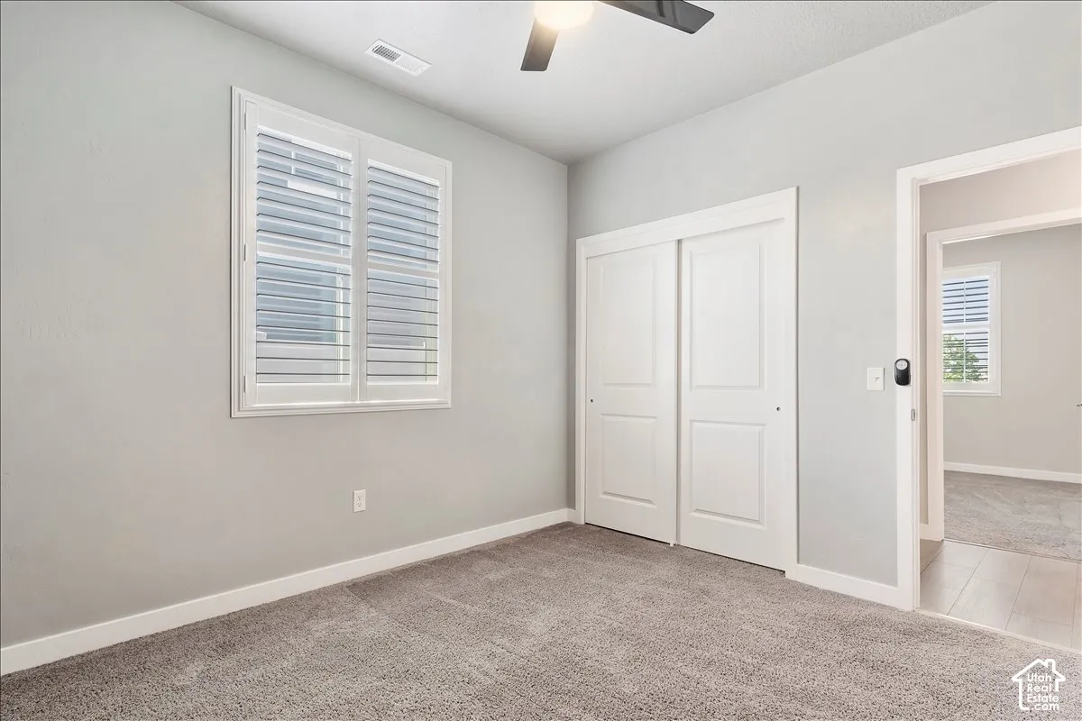 Room featuring carpeting, a ceiling fan, a window with plantation shutters, and a sliding door closet