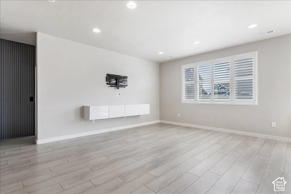 Recessed lighting, light gray walls, wood-finish flooring, white window shutters, and a built-in white floating media console