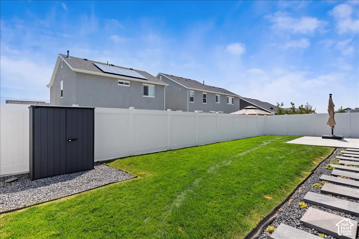 Expansive backyard featuring a lush lawn, white privacy fencing, a concrete patio, and a dedicated storage shed