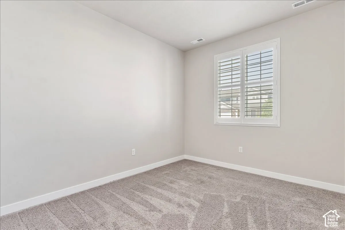 Neutral wall finishes, white trim, window with plantation shutters, and light-toned carpet