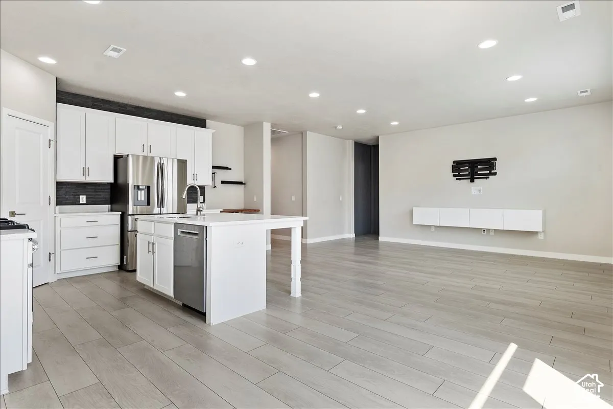 Open-concept living area featuring wood-finish flooring, recessed lighting, and a kitchen with white cabinetry, a center island, and stainless steel appliances
