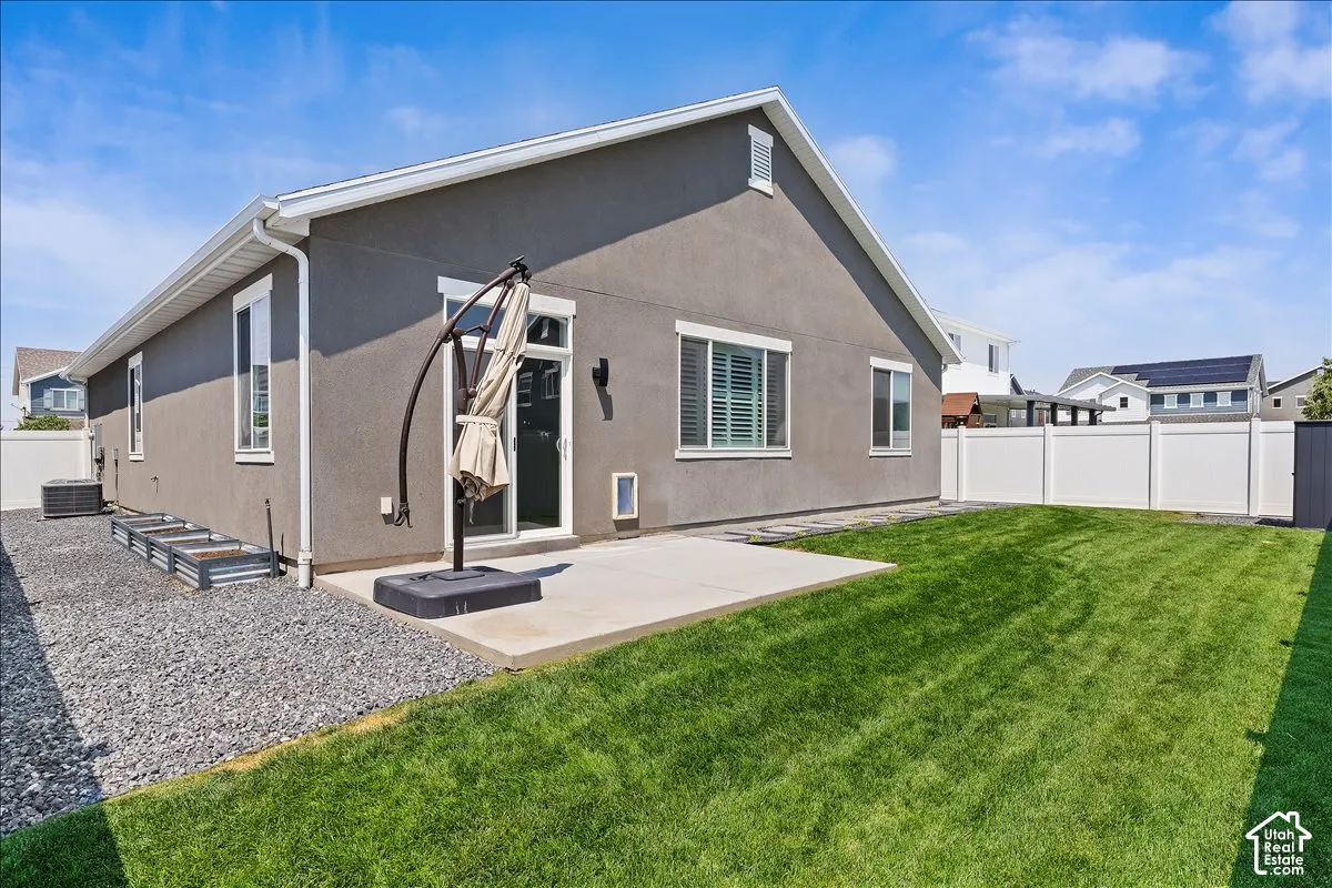Expansive backyard featuring a manicured lawn, concrete patio, and white vinyl fencing