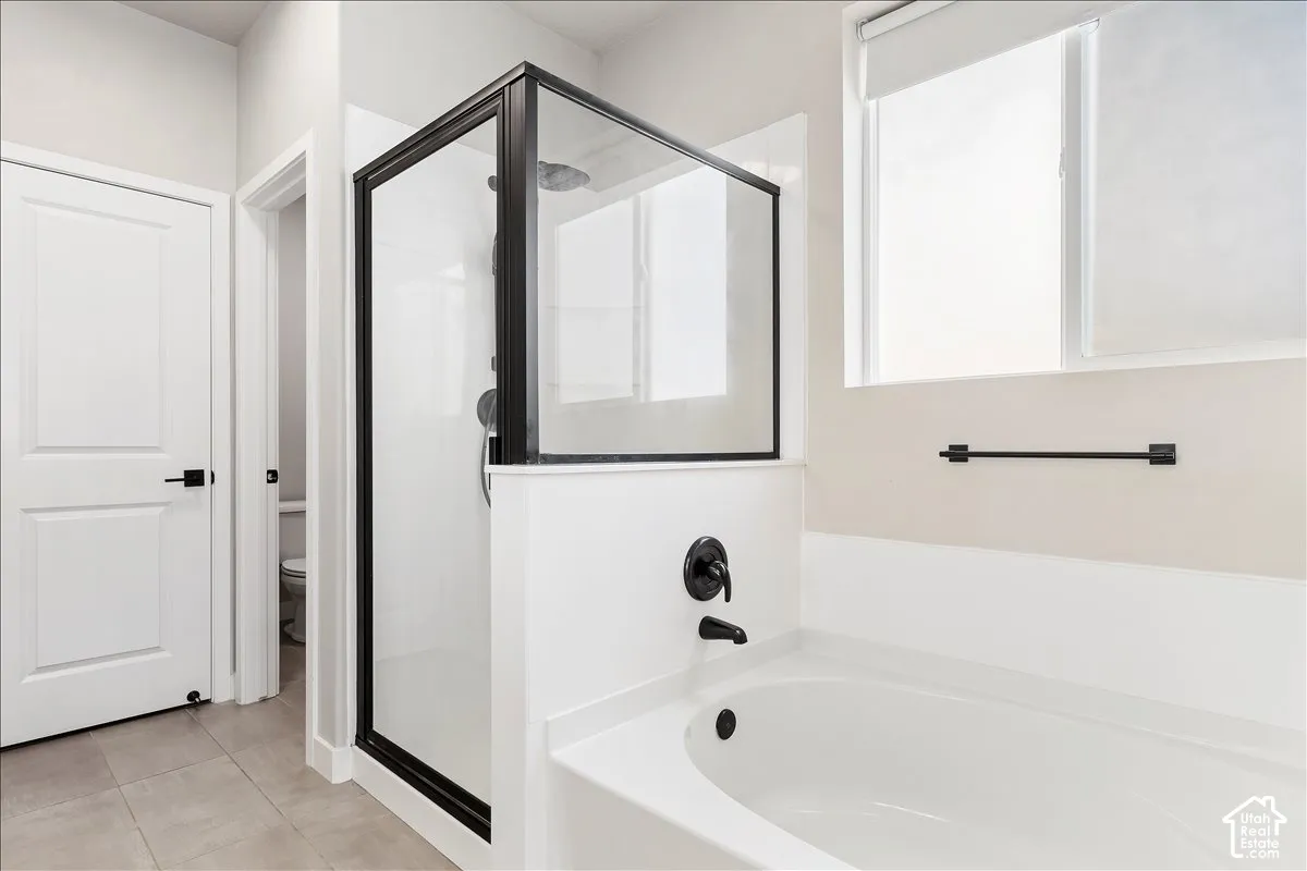 Recessed bathtub with matte black fixtures, glass-enclosed shower, and tile flooring