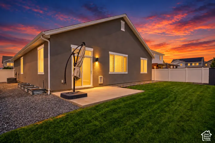 Expansive backyard featuring a manicured lawn, concrete patio, sliding glass door, and a privacy fence