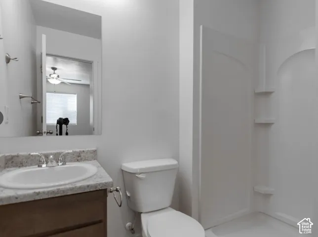 Bathroom featuring a single vanity with an integrated sink, a built-in shower stall with shelving, and a toilet