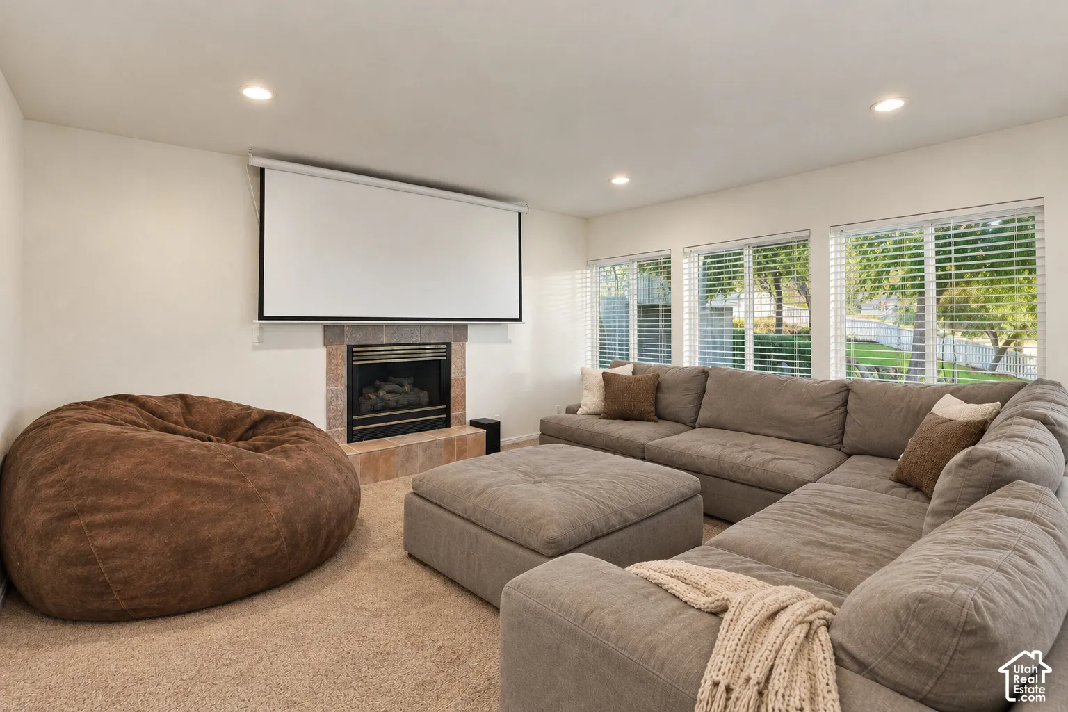 Integrated projection screen, tiled fireplace with black insert, recessed lighting, and multiple windows with blinds
