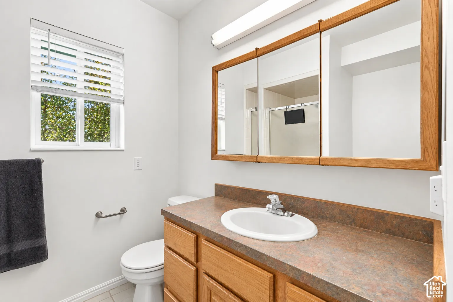 Bathroom featuring a single window, a wooden vanity with integrated sink, and a multi-panel mirrored medicine cabinet