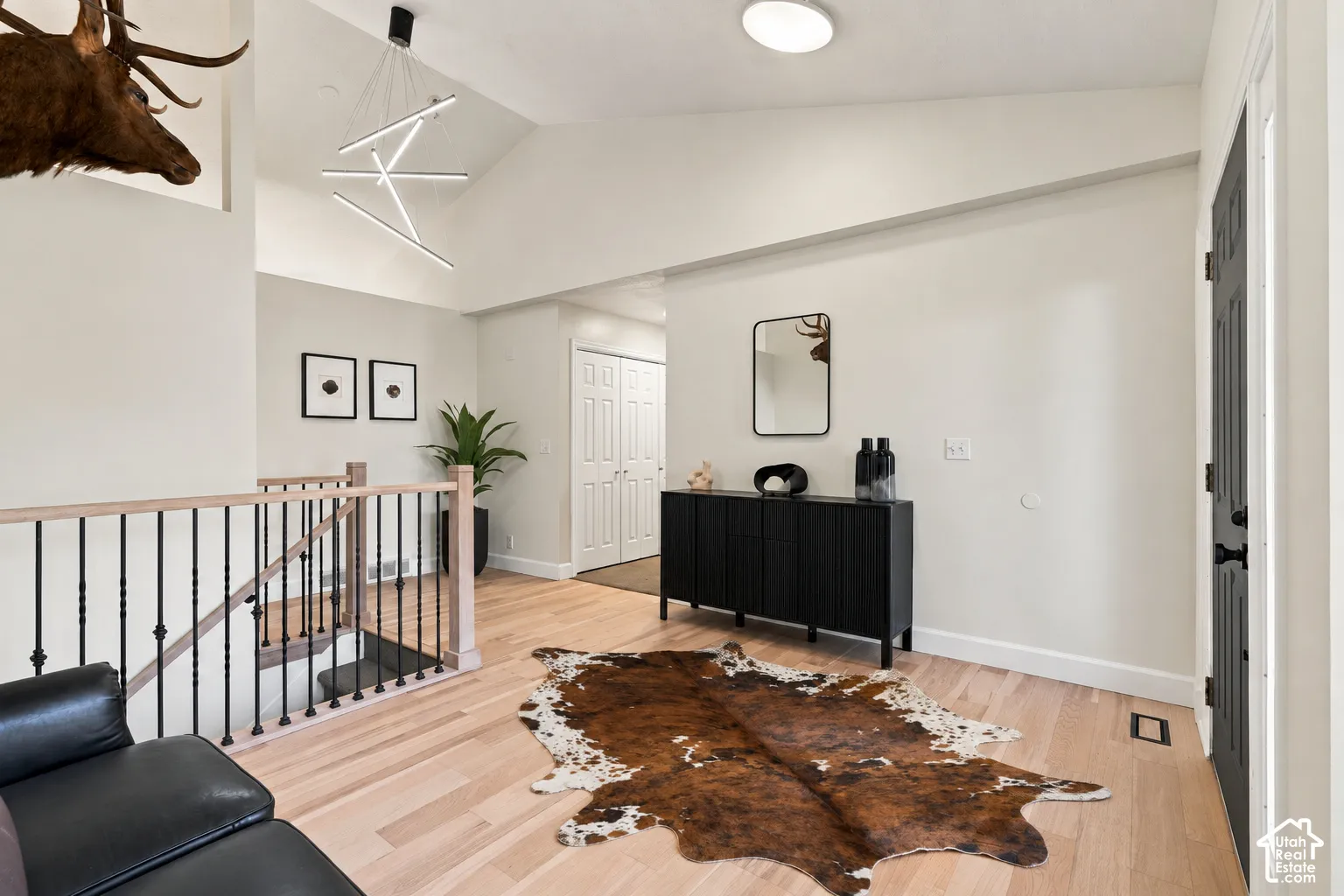 Vaulted ceiling with a contemporary linear chandelier, light wood-finish flooring, black wrought iron stair railing, and a built-in black console cabinet