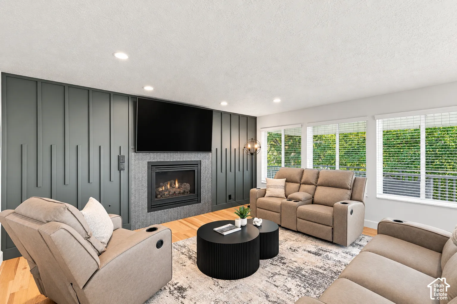 Recessed lighting, wood-finish flooring, a contemporary fireplace with a textured surround, and a paneled accent wall