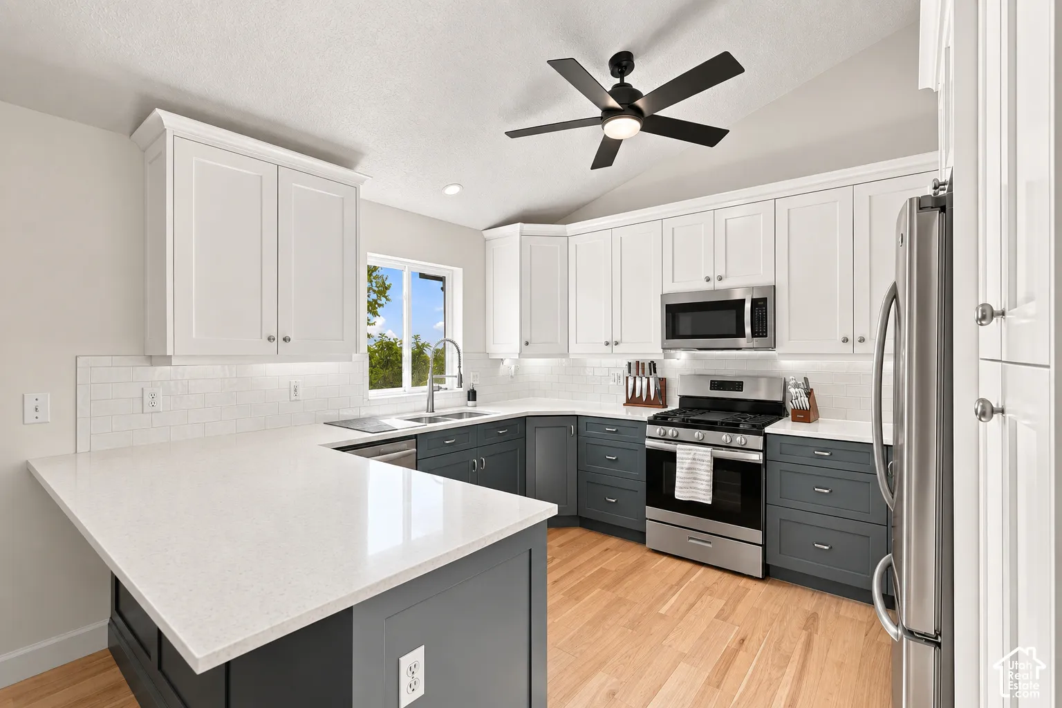 Kitchen featuring two-tone cabinetry, stainless steel appliances, light-toned countertops, wood-finish flooring, and a ceiling fan