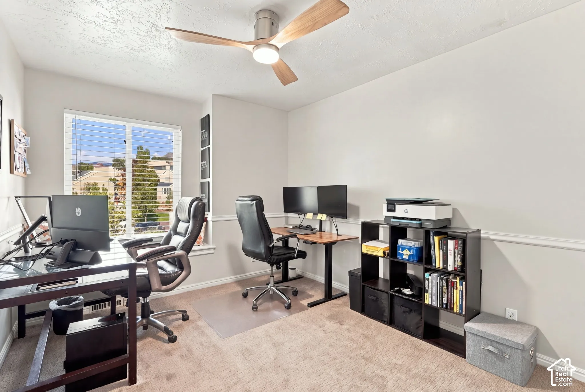 Carpeted room featuring a ceiling fan with integrated lighting, a large window with horizontal blinds, and neutral-toned walls with a chair rail