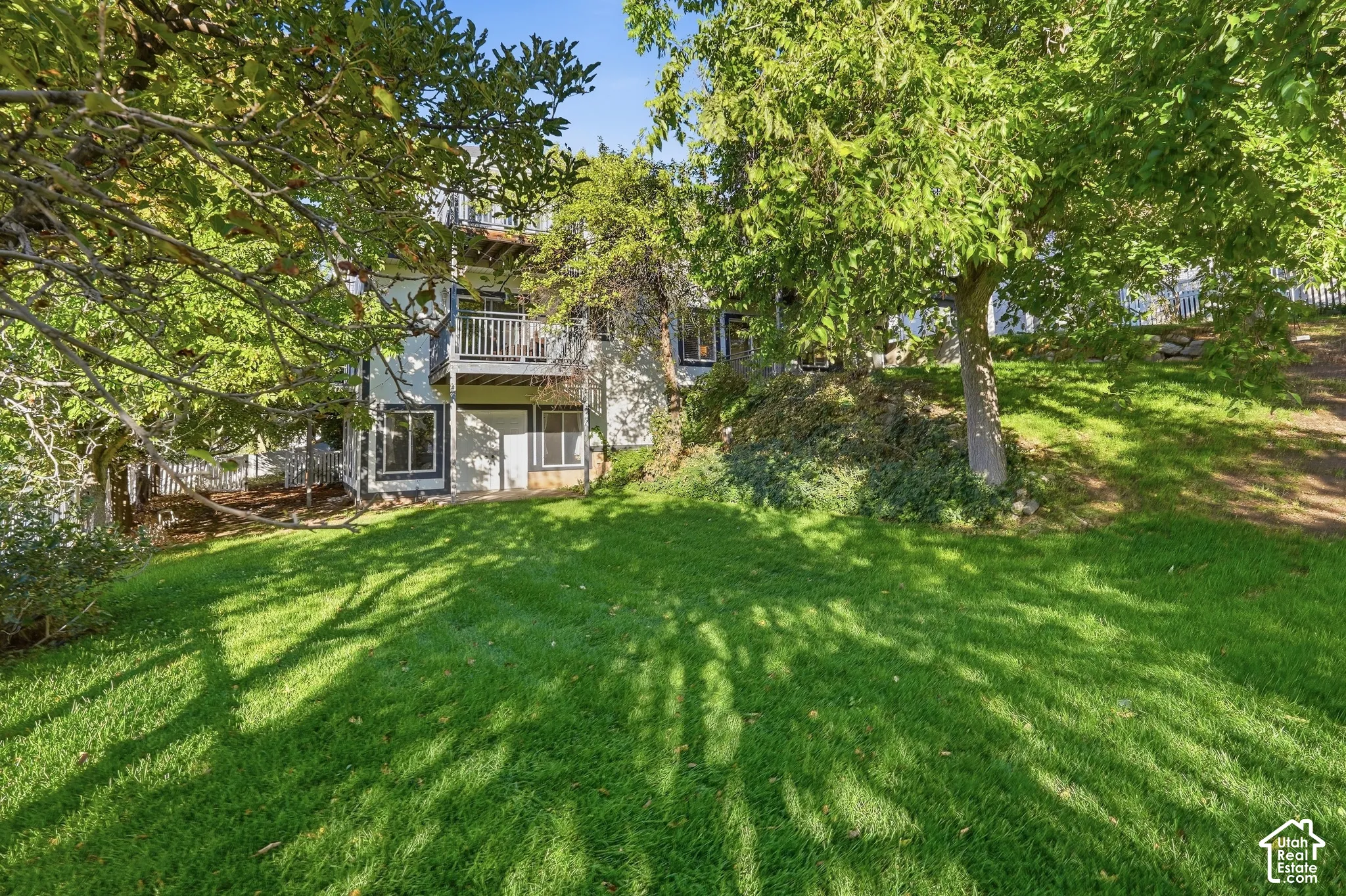 Expansive grassy yard with mature trees, a multi-level exterior, and a top-level balcony with white railings