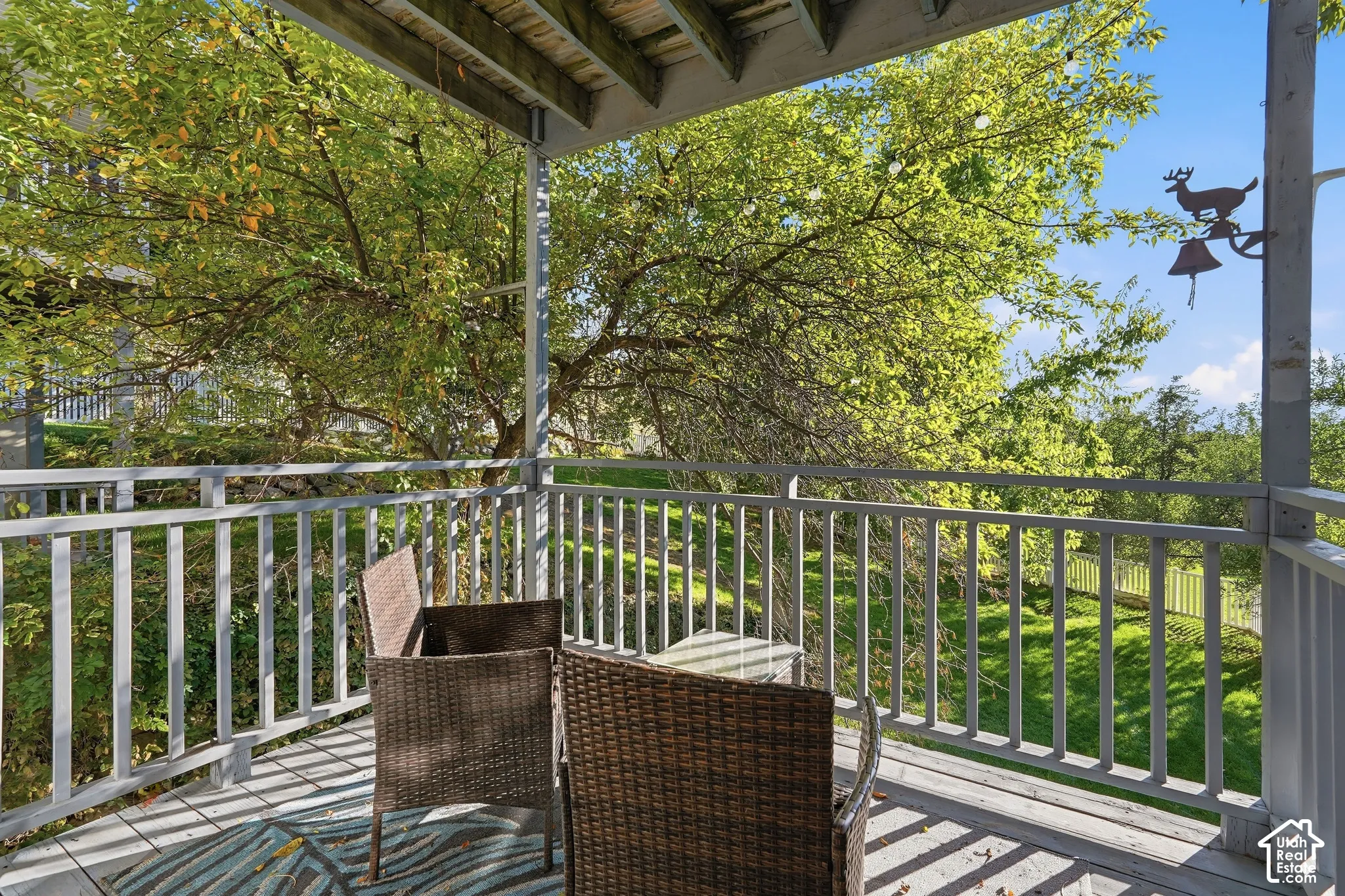 Covered wood-plank deck with painted wood railings, overlooking a sloped lawn and mature trees