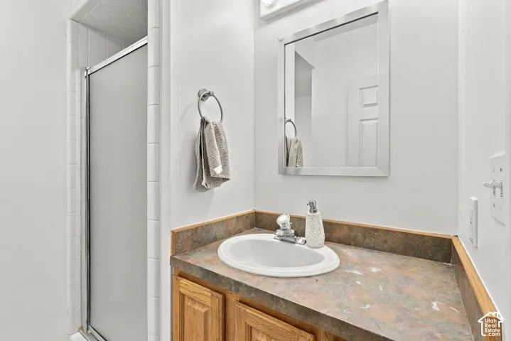 Enclosed shower with frosted glass, wood-finish vanity with an integrated sink, and an unframed rectangular mirror