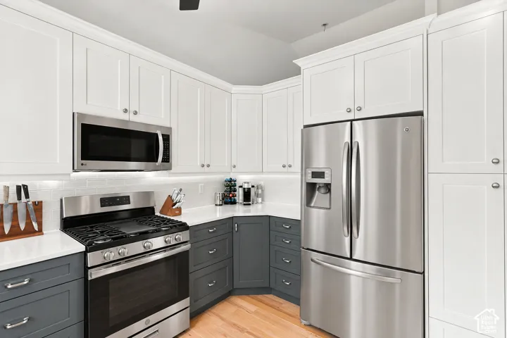 White shaker cabinetry, stainless steel appliances, white subway tile backsplash, light wood-finish flooring, and white countertops