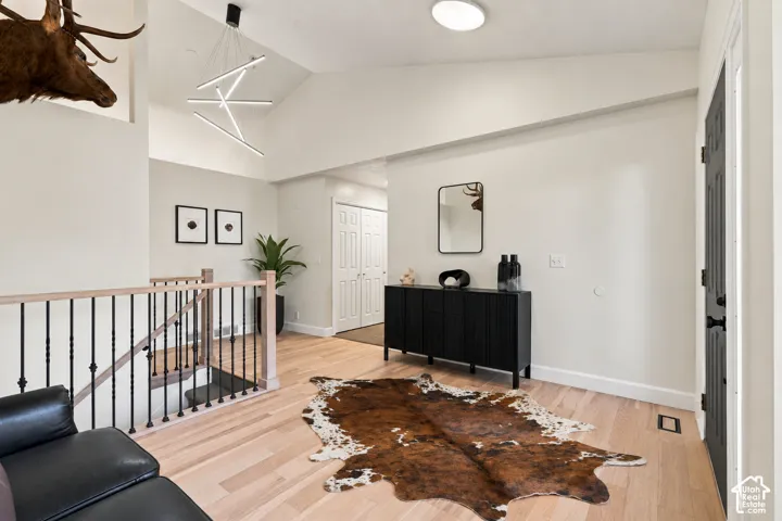 Vaulted ceiling with a contemporary linear chandelier, light wood-finish flooring, black wrought iron stair railing, and a built-in black console cabinet