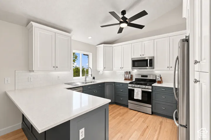 Kitchen featuring two-tone cabinetry, stainless steel appliances, light-toned countertops, wood-finish flooring, and a ceiling fan