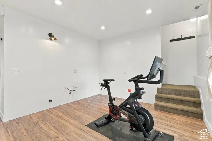 Dedicated fitness room featuring wood-finish flooring, recessed ceiling lighting, and built-in wall-mounted storage