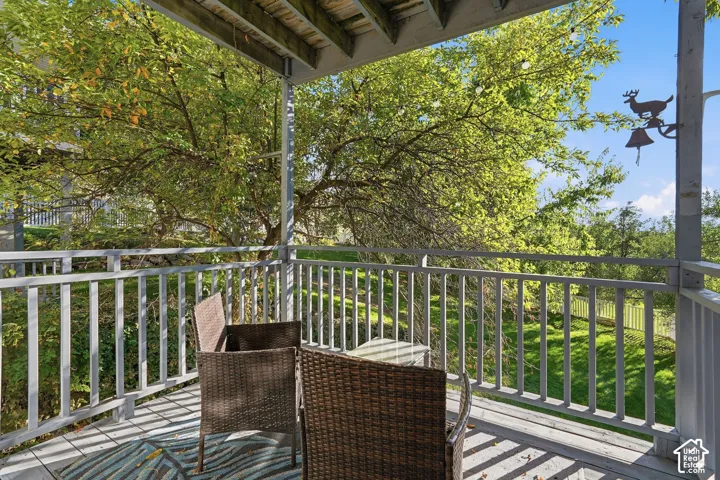 Covered wood-plank deck with painted wood railings, overlooking a sloped lawn and mature trees